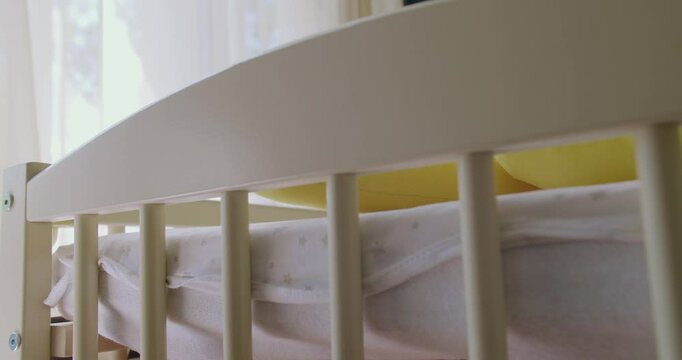 Wooden crib with protection borders in nursery room. Modern baby bed with soft toy and bedding. Closeup of soft toy lying in baby bed in nursery room. Preparing room for newborn.