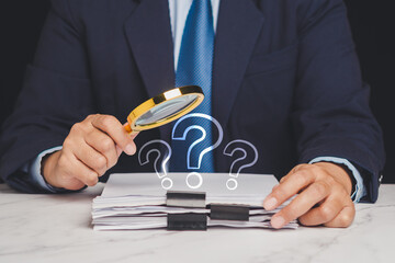 Business professional inspecting paperwork with magnifier and question marks.