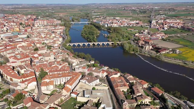 Picturesque aerial view of Zamora city overlooking brownish tiled roofs of residential buildings and ancient arched bridge over Duero river on spring day, Spain 