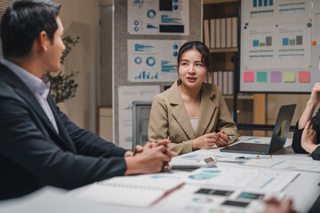 Business team collaborating in a modern office, analyzing financial data and discussing strategies for a new project while examining growth graphs on laptops and documents