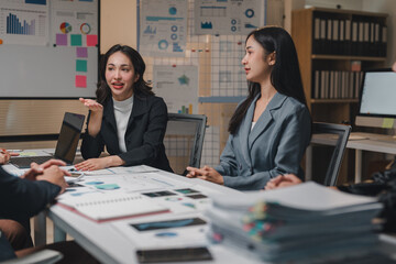Businesswomen leading a meeting with colleagues, discussing charts and business strategy in a modern office, fostering collaboration and teamwork for achieving company goals