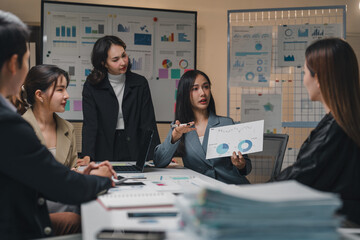 Young asian businesswoman leading a meeting with her team, presenting charts and pie graphs to her coworkers in the office, discussing financial results and business strategies