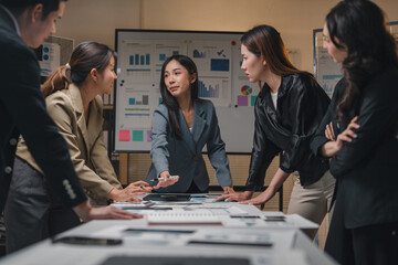 Group of diverse businesspeople leaning on a table analyzing financial reports, working together to achieve business goals in a modern office at night