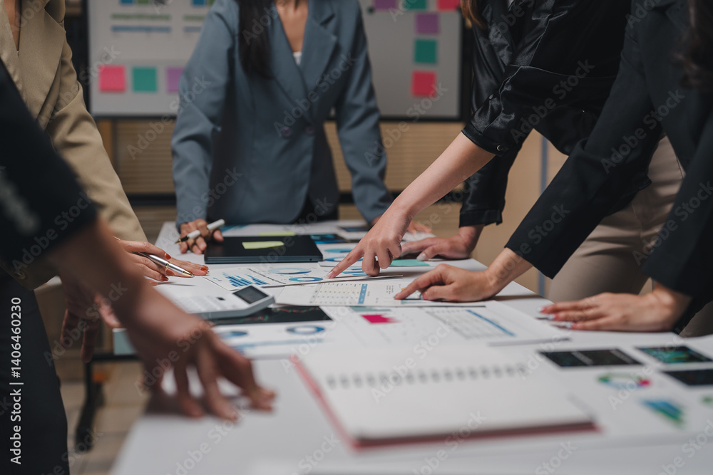 Poster businesswomen are pointing at financial charts and graphs spread out on a desk, collaborating on dat