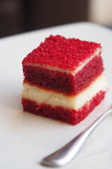 Red velvet cake square served on white plate with fork