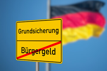 Flagge von Deutschland und Ortstafel, die auf das Ende vom Bürgergeld und Anfang der Grundsicherung hinweist 