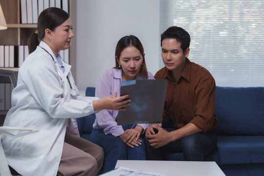Female doctor explaining radiography results to a worried young couple sitting on a sofa in a hospital office during an important medical consultation about their health