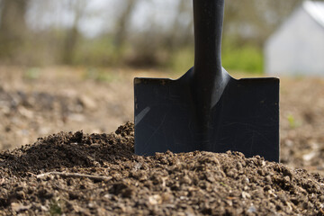 Black shovel stands in a pile of fertile soil, ready for gardening in a sunny backyard.