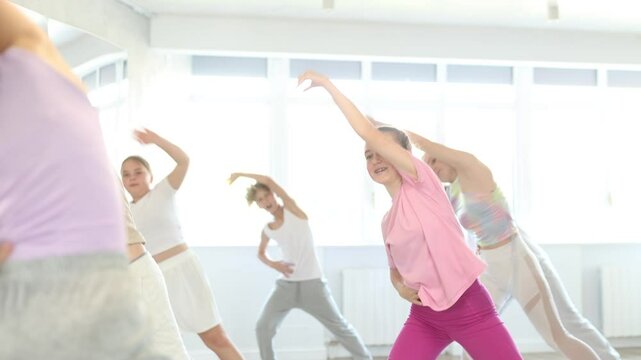 Girl teen performs modern dances repeats movements of unrecognizable teacher together with friends during lesson at choreographic school. Hobbies, active pastime