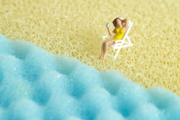 Miniature people toy figure photography. Girl relaxing at beach chair in front of wavy beach