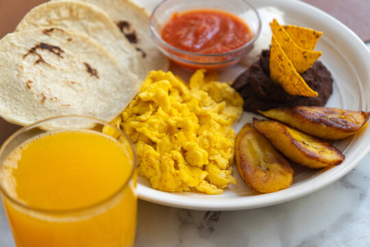 Close-up of a traditional Guatemalan breakfast of fried eggs, beans with nachos, sour cream, fried plantains, orange juice, and tortillas