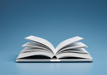 Fototapeta premium Open book with white pages resting on a flat surface against a blue background in a studio shot