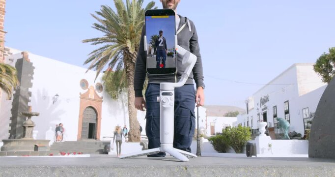 A Man Using 3-axis Gimbal Stabilizer With Built-in Selfie Stick And Tripod In The City. Close-up Shot