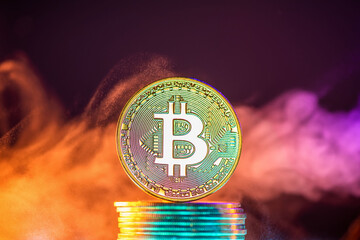 Bitcoin cryptocurrency coin standing on a stack of coins surrounded by colorful smoke on a dark...