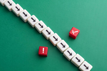 Representing disruption and deviation, a single file of white dice with black downward arrows is offset by two red dice featuring a white exclamation mark and a cross, all against a solid green backgr