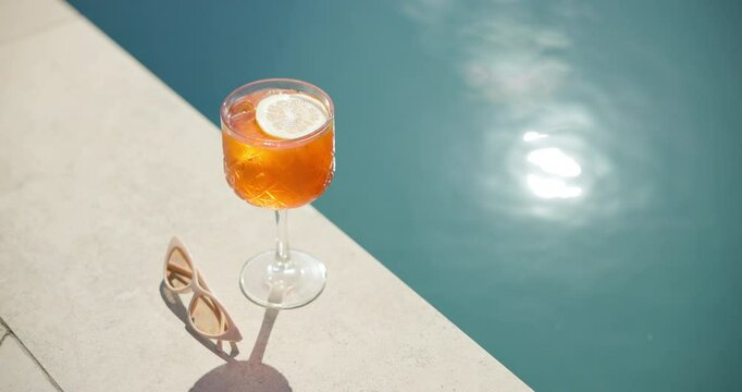 Swimming pool, glass and cocktail with sunglasses for holiday, summer vacation or relax outdoor. Water, alcohol and drink at hotel resort for tourism, travel and luxury with fresh lemon in top view