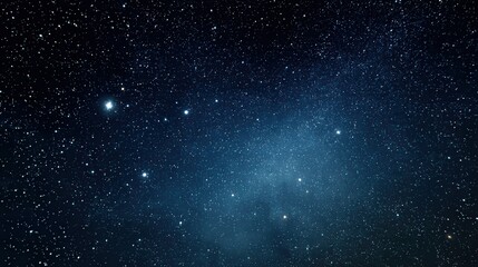 Fototapeta premium A vast expanse of a starry night sky fills the scene, with countless twinkling stars scattered across a deep blue backdrop. The stars vary in brightness, creating a sense of depth.
