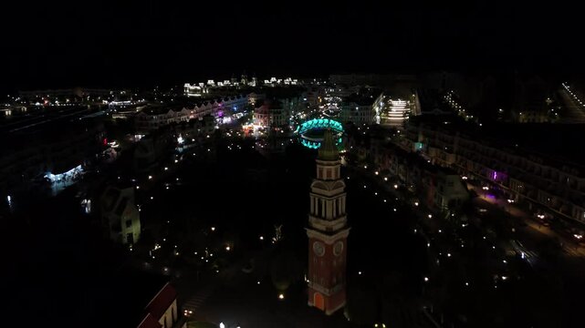 Close aerial shot of the Vietnamese night sky, the enchanting Grand World comes alive with vibrant illumination, trees lavishly adorned with a dazzling array of colorful lights. Clock tower.
