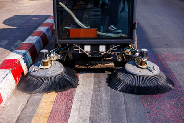 street cleaning machine sweeping along colorful painted lines on city road beside red and white curb under bright sunlight

