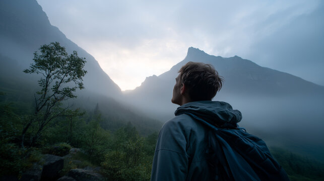 Man looking up at misty mountain peaks landscape