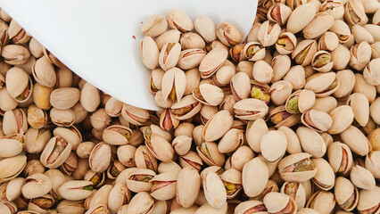 White scoop picking pistachios from pile of roasted pistachios