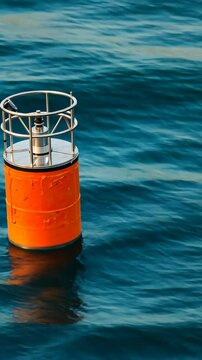 Bright orange cylindrical buoy with stainless steel frame floating in open, deep blue water, showing calm ripples.