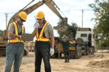 Two construction workers in hard hats and reflective vests discussing blueprints at an industrial...