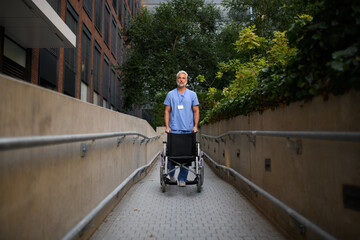 Portrait of male caregiver pushing empty wheelchair.