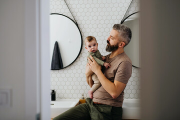 Portrait of father holding baby son in arms.