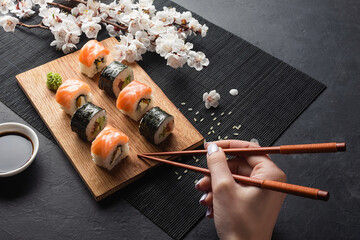 Set of sushi, maki rolls, hand with chopsticks and branch of white flowers on stone table