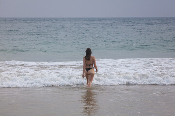 A woman is walking on the beach in a bikini