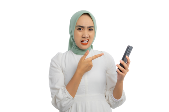 Beautiful young Asian woman in green hijab and white blouse pointing finger at mobile phone with confused expression isolated on transparent background