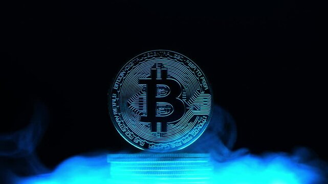 Glowing bitcoin is standing on a stack of coins surrounded by blue smoke on a dark background with copy space, representing the mysterious nature of cryptocurrency