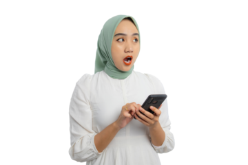 Shocked young Asian woman in green hijab and white blouse holding smartphone and looking aside at copy space, showing amazed expression isolated on transparent background