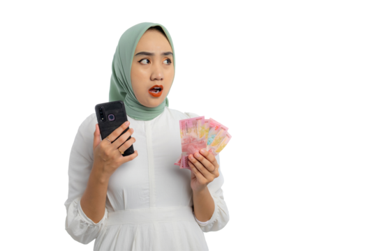 Beautiful young Asian woman in green hijab and white blouse holding money and mobile phone, looking aside at copy space with shocked expression isolated on transparent background