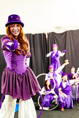 Smiling circus artist wearing purple costume and holding hula hoop, reaching out hand with other...