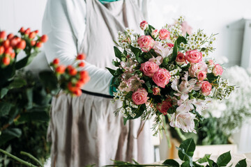 Florist arranges pink lilies and roses into a lush floral display on a studio worktable. Women-owned business, florist at work, independent creator, creative entrepreneur