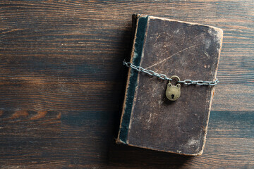 Metal chain and padlock around old book on wooden background, closeup, top view. Copy space for text