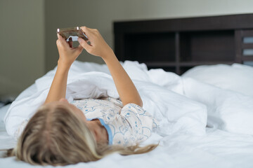 girl lies in bed with white sheets and plays on phone