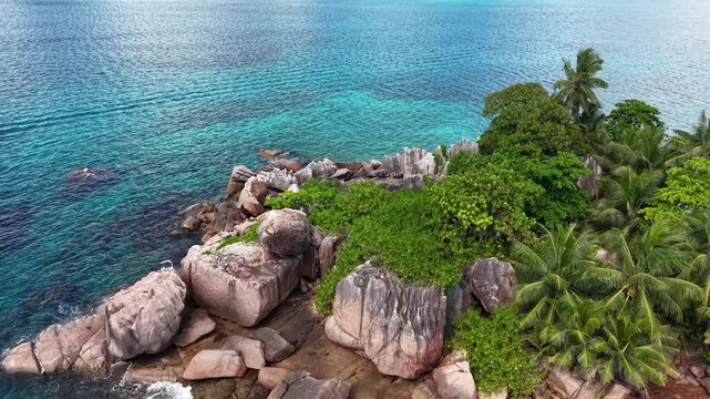Praslin Island, Seychelles, featuring a tiny rocky islet with palm trees surrounded by crystal-clear turquoise ocean and a nearby sailboat.
