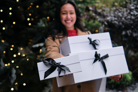 Smiling woman holding gift boxes outdoors during festive holiday season