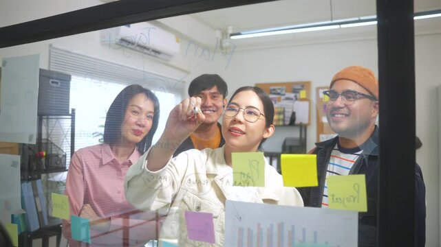 Diverse group Asian business team planning with sticky notes and new ideas on a glass whiteboard, Business people brainstorming strategy and new ideas concept.