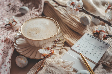 April 2025 calendar with April 20 marked, next to a golden pen, cup of coffee, blooming spring...