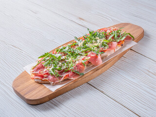 Pizza Parma. Pizza Prosciutto. Freshly baked Pizza Parma with a thin crispy crust, topped with prosciutto, arugula, and shaved Parmesan. Served on a rustic wooden board with a dark background