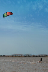 A man, an athlete, rides kitersurfing on a blue pore. Beach, active recreation. Sunset competitions, parachute, board. High quality photo