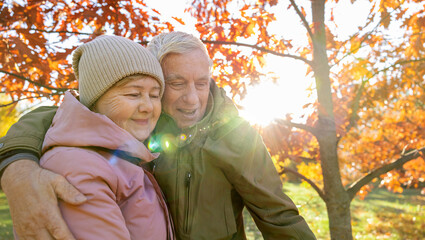 Elderly couple cuddling in a sunny autumn forest