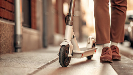Obraz premium Modern electric scooter parked on city sidewalk, compact and eco-friendly urban transportation for sustainable mobility and green lifestyle concept.