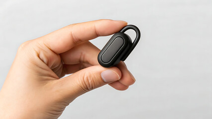 A hand holds a small black Bluetooth earpiece ideal for calls and music listening