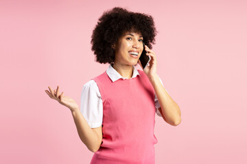 Young Latin woman talking on phone and gesturing on pink background