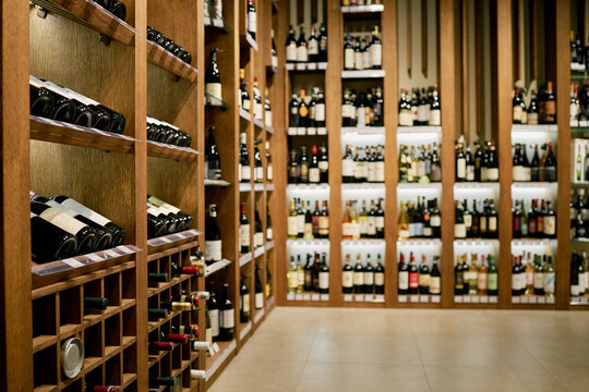 Numerous bottles organized in wine cellar with wooden shelves creating an elegant ambiance. Well-lit environment highlighting diversity of wine brands and types